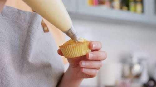 Woman Frosting Cupcake with Cream in Bright Kitchen