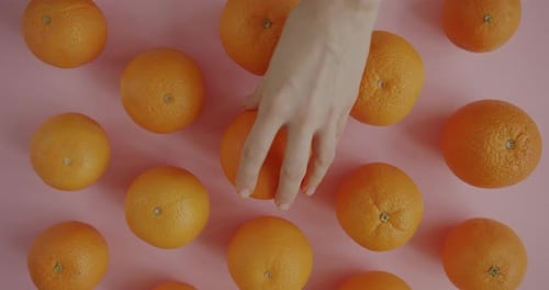Top View of Female Hand Taking Fresh Organic Orange From Pink Table