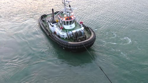 A tugboat is attached to the stern of a ship and floats behind it.