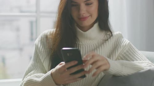 Smiling Woman Using Mobile Phone on a Sofa
