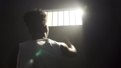 Häftling greift durch vergittertes Fenster in der Gefängniszelle dem hellen Sonnenlicht entgegen