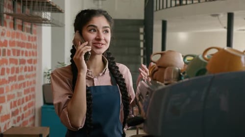 Smiling Indian Female Barista Waitress in Apron Talking on Phone Behind Cafeteria Counter Remote