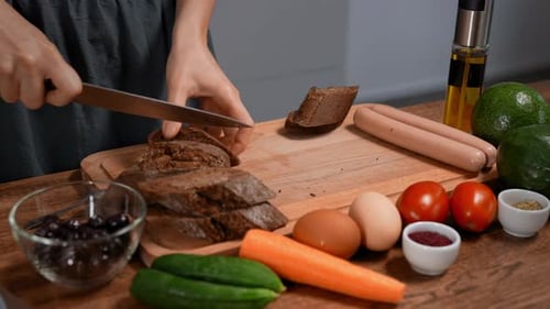 Woman Cutting Bread on Wooden Cutting Board in Kitchen