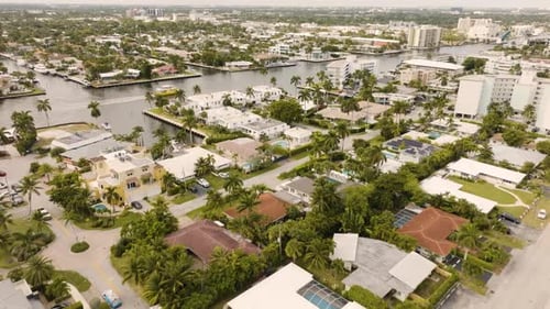Tropical beach town aerial over vacation homes with pools and palm trees approaching water ways