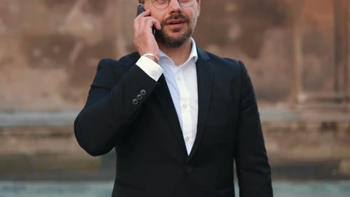 Cheerful Caucasian Businessman Wearing Glasses Standing in City and Talking on Smartphone Handsome