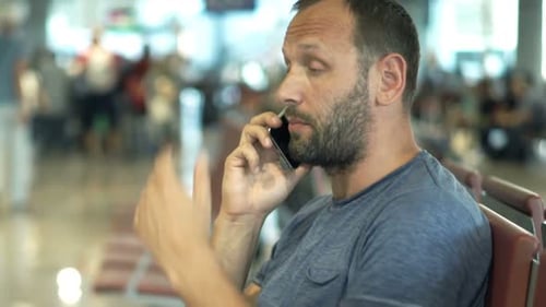Frustrated man on cellphone awaiting late plane in busy airport terminal