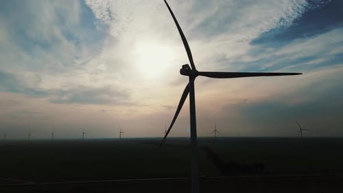 Silhouette of a windmill at sunset, sunrise with cloudy sky, more windmills in the background, blue