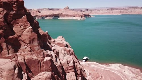 Drone shot flying past large red rocks on Lake Powell to reveal a houseboat and the lake