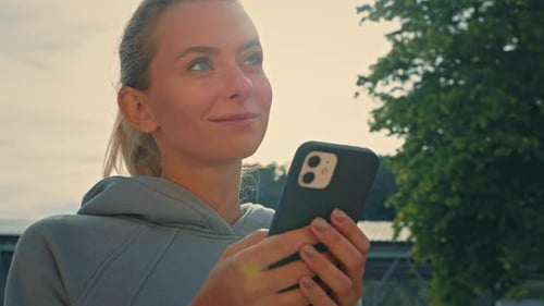Smiling Woman Holds Phone Outside in the Park