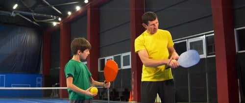 A woman and a child playing pickleball on a blue, inside court