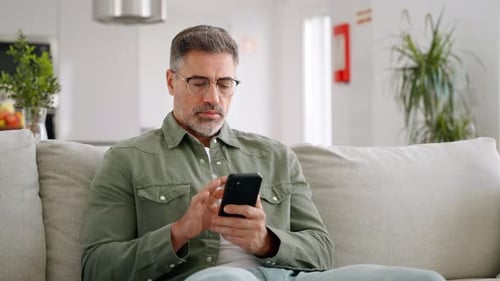 Man Uses Smartphone Relaxing on Couch Indoors