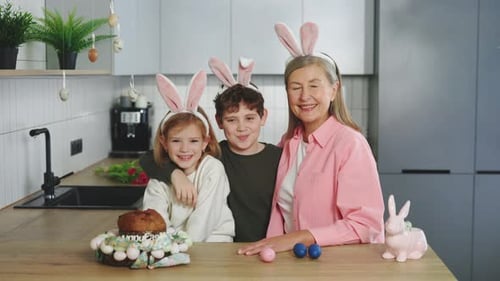 Großmutter und ihre Enkelkinder verbringen Zeit miteinander und tragen Hasenohren und sitzen am Tisch in
