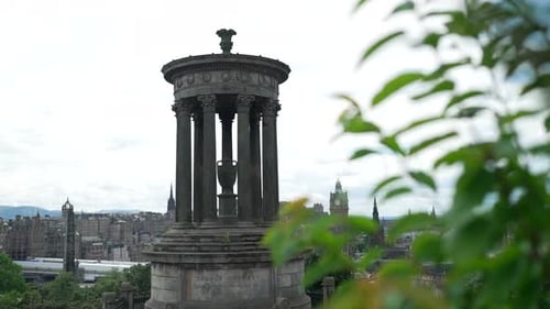 Handheld slider past blades of grass reveals dugald tower in Edinburgh