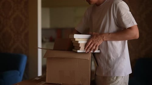 Side View of Unrecognizable Man Packing Books Into Cardboard Box Preparing for Move Organizing and