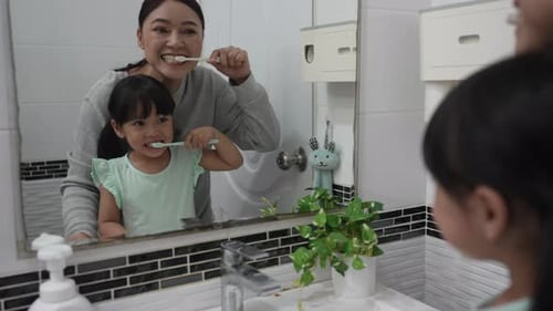 Woman and Child Brush Teeth Together in Bathroom