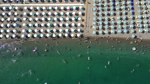 A drone flies over a beautiful beach with umbrellas. People sunbathe and swim.