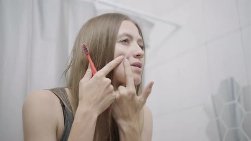 Young Woman Checking Face in Bathroom Mirror
