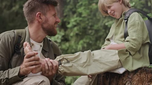 Man Examines Boy's Foot in the Forest