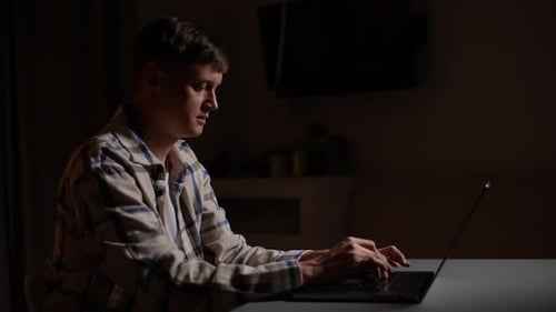 Side View of Focused Busy Young Man Working Browsing on Laptop Computer at Late Night at Home