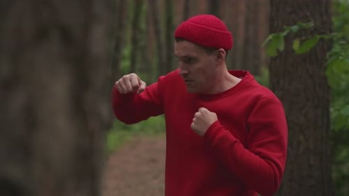 A Man is Seen Practicing Boxing Moves in a Serene Forest He is Wearing a Red Outfit and Appears to