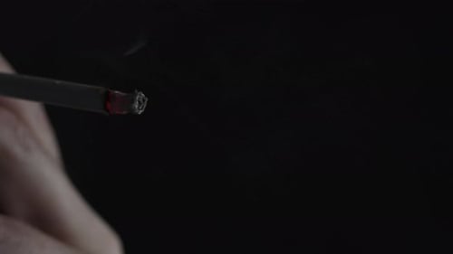 Hand Holds Lit Cigarette in Dark Close Up