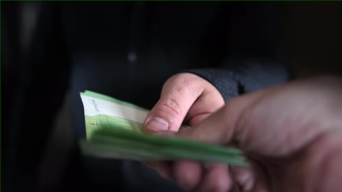 Man hand holds out stack of hundred euro bills to another person, close-up on blurred background