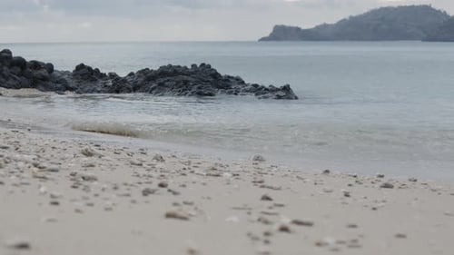 Ocean waves crashing on beach and black rocks on an island