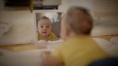 Adorable Baby Looks in Mirror Lying on Rug