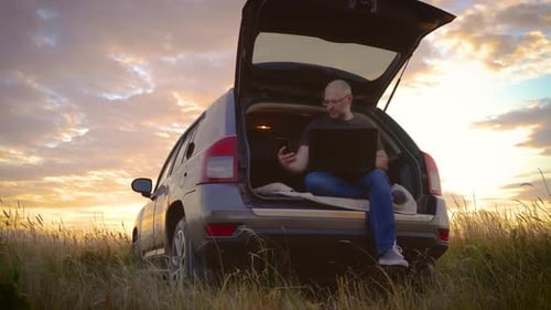 Freelancer caucasiano careca trabalhando remotamente com laptop e smartphone sentado no carro