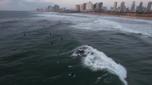 Aerial view of many surfers, riding waves with Tel Aviv skyline background - tracking, drone shot