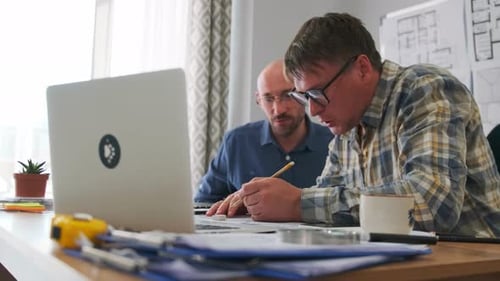 Architect and Engineer Reviewing Blueprints in Office
