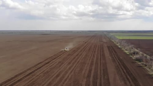Blue tractror planting sunflower with yellow planter on the cultivated field in Ukraine