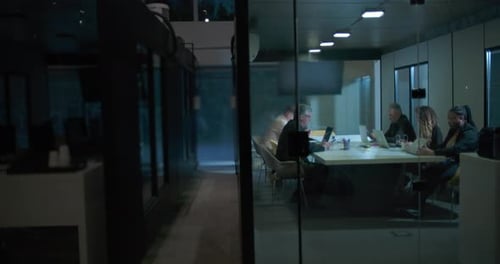 Wide view of diverse team working late in glass boardroom during corporate night shift