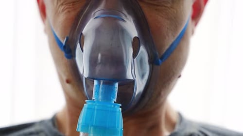 Close Up View of Unhealthy Man Wearing Nebulizer Mask Breathing in Home Health Medical Equipment and
