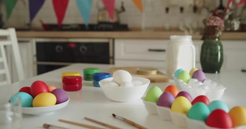 Multicolored Easter Eggs Paint Jars and Brushes on a Kitchen Table