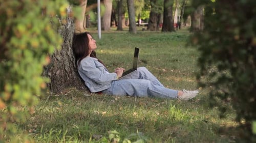 Eine junge Frau, die in einem Stadtpark an einem Computer arbeitet, während sie auf einer Decke sitzt
