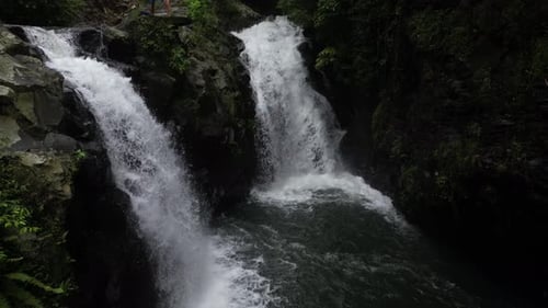 Two waterfalls with rocky cliffs and jungle in the surrounding area, aerial.