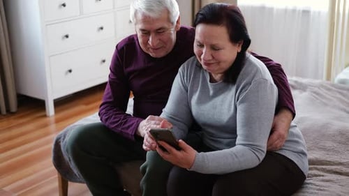 Senior Couple Relaxing Together Using Mobile Phone Indoors