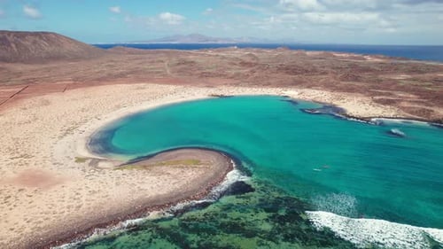 4K aerial drone view of Playa de la Concha de Lobos, Fuerteventura, featuring turquoise waters, rock