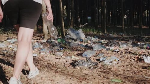Woman Walking Through a Pile of Garbage in the Forest and Throwing a Bottle