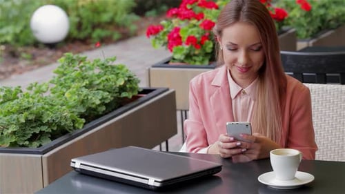 Young Woman Joyfully Using Her Smartphone in a Vibrant Cafe