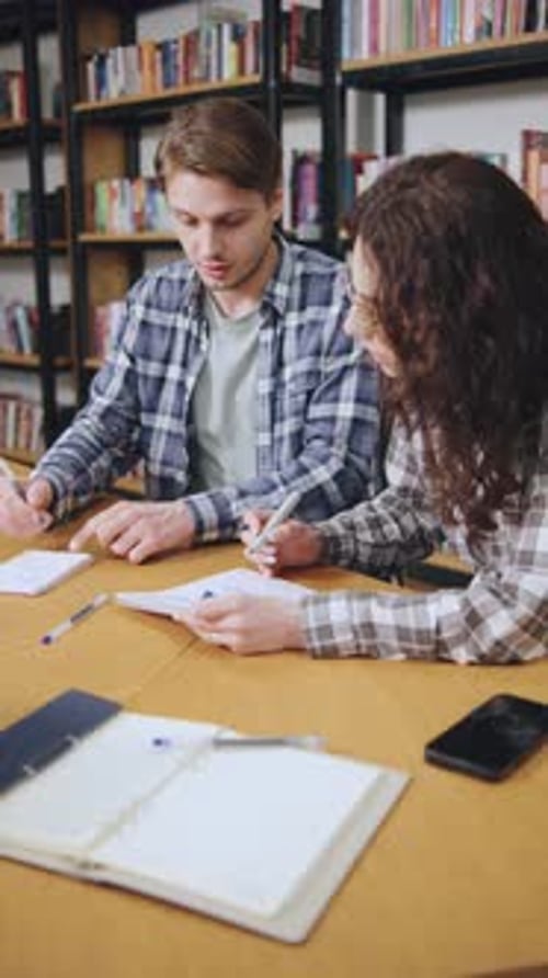 Vertical Video of Students Collaborate on a Project at a Study Table Surrounded By Books in a