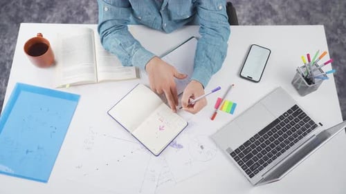 Person Working at Desk with Laptop and Notebook