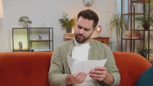 Stressed Caucasian Young Man Sitting on Sofa Reviewing Unpaid Debt Bills and Throwing Up in Air