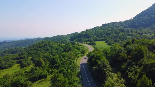 Cinematic drone captures shot of beautiful empty road. Camera flies behind car