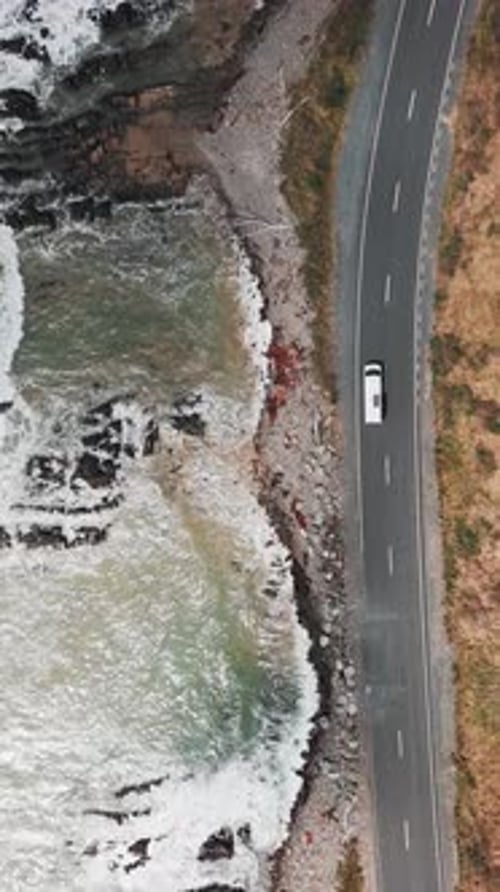 Vertical drone shot of a camper van driving along ocean in Molyneux Bay near Kaka Point in Otago