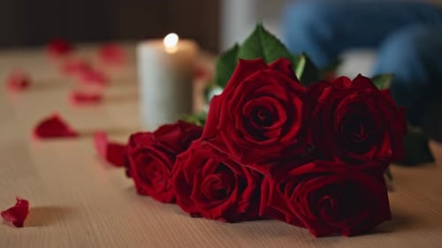 Schöner Rosenstrauß, der auf dem Tisch neben brennenden Kerzen liegt, rote Blumen aus nächster Nähe