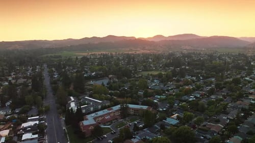 Flying over green city of Napa, California, USA. Mountainous skyline at backdrop of pink skies.