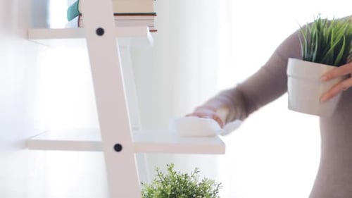 Woman Cleans Modern White Bookshelf in Bright Home