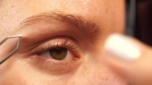 Woman Shaping Eyebrow with Tweezers Close Up